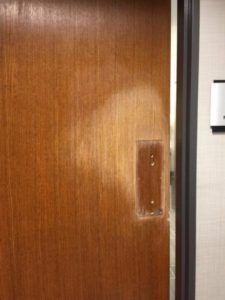 A restroom door with the color and finish worn off down to the wood